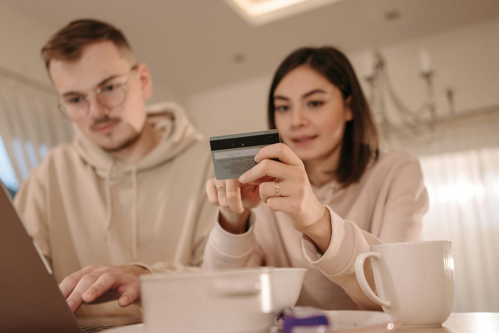 Young couple shopping online using a laptop and credit card at home, enjoying a cozy indoor setting.